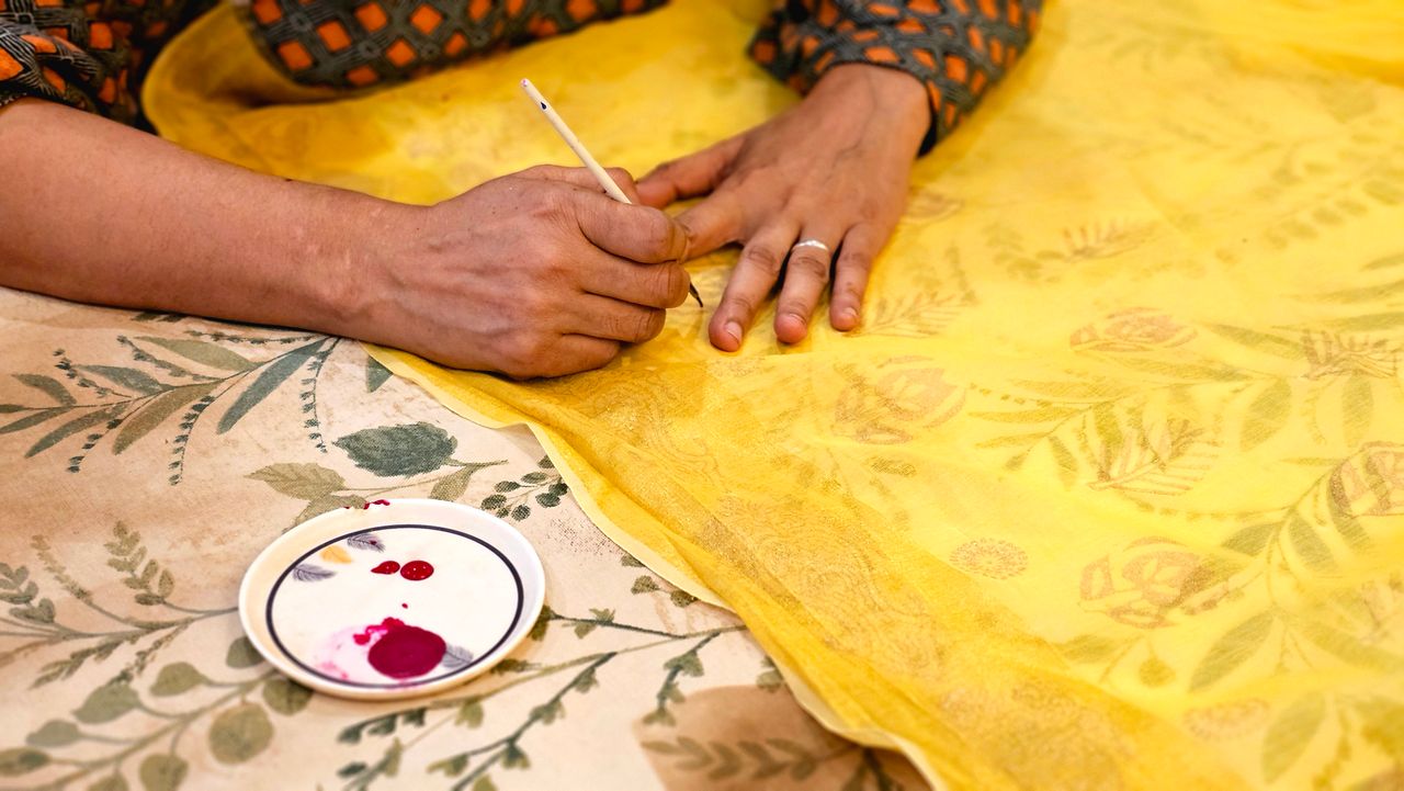 Close-up of hands painting on fabric with intricate design details.