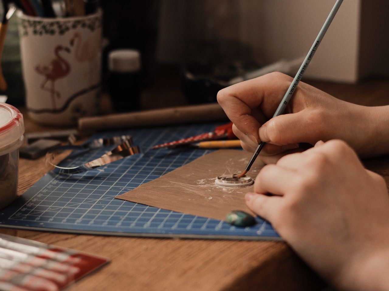 A close-up view of a person crafting jewelry using precision tools and clay indoors.